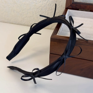 Detail view of a black satin headband with handmade bows on a vintage wooden jewelry box