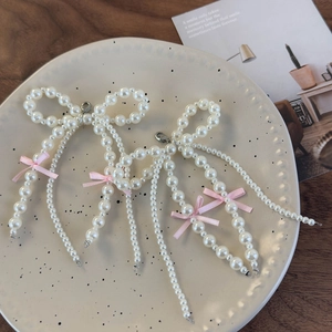 Detailed close-up of pink ribbon and pearl bow charms with silver lobster clasps