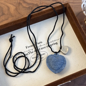 Detalle del colgante de corazón en denim azul y placa de plata grabada en cordón trenzado