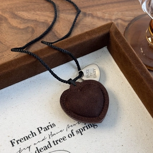 Detalle del colgante de corazón en ante con costuras y etiqueta metálica grabada en cuerda