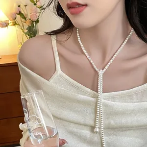 Detailed view of elegant long Y-shaped pearl necklace on model with warm home decor