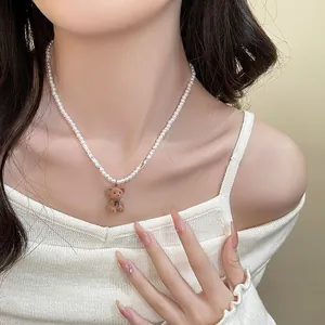 Détail d'un collier de perles blanches avec pendentif ourson marron et petit nœud noir