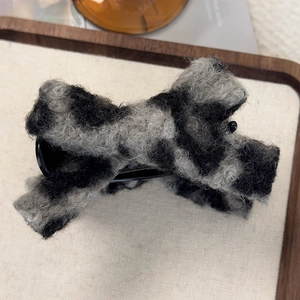 Close-up of black and grey faux shearling claw clip with soft fluffy texture on wood base