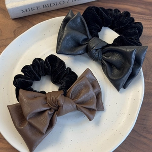 Brown and black leather bow hair scrunchies on a white porcelain plate with wooden background