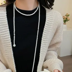 Detailed view of layered long pearl necklace with large round pendant on a knitted sweater