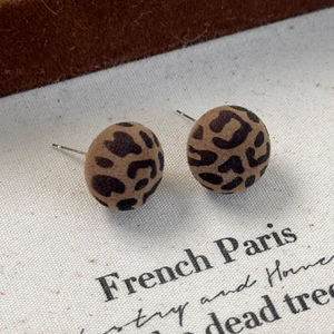 Detailed close-up of vintage leopard print flocking button stud earrings on rustic fabric
