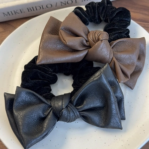 Dual-layer leather bow scrunchies in brown and black on a white ceramic plate
