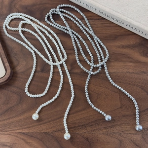 Detail of long pearl necklaces in white and grey displayed on dark wood surface