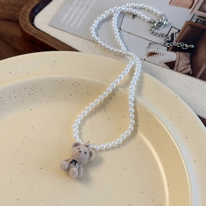 Gros plan d'un collier de perles avec pendentif ours en velours gris sur une assiette