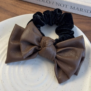 Detail of deep brown leather bow and black velvet scrunchie on ceramic plate