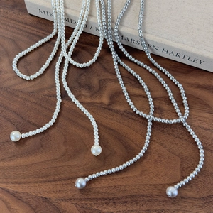Detailed view of long white and silver grey pearl lariat necklaces on wooden surface