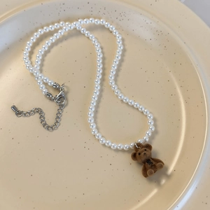 Vue détaillée du collier de perles blanches avec pendentif ours en velours et fermoir