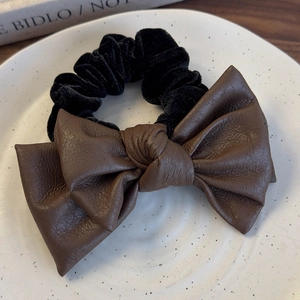 Detailed macro of brown leather bow hair tie and black velvet scrunchie on ceramic dish