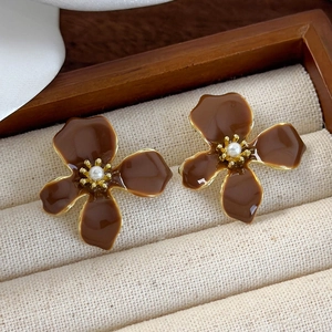 Detailed close-up of brown enamel flower earrings with pearls on a wooden jewelry tray