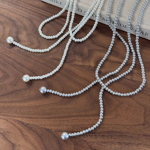 Detail of long layered white and grey pearl necklaces on a dark walnut wood background