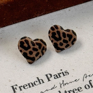 Close-up of heart-shaped leopard print flocked earrings on a neutral vintage fabric