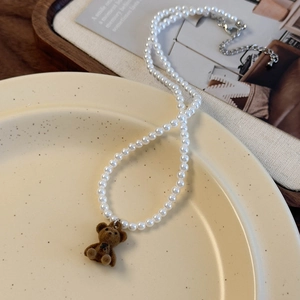 Vue détaillée d'un pendentif ours en velours marron sur un collier de perles blanches polies