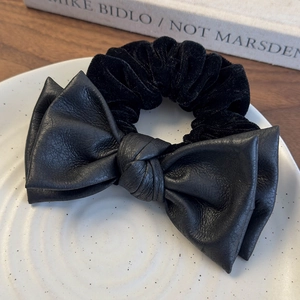 Detailed view of black leather bow hair tie and velvet scrunchie on ceramic plate