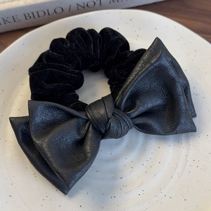 Close-up of black velvet scrunchie with leather bow on a decorative ceramic tray