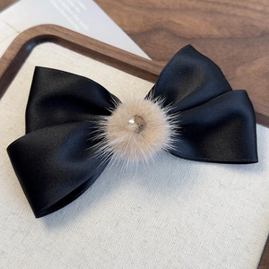 Dettaglio elegante fermaglio per capelli in raso nero con pompon beige e cristallo centrale
