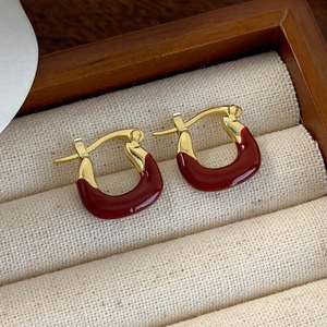 Close-up of vintage U-shaped earrings with dark red glaze and gold-plated finish