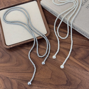 Detail of long pearl necklaces in white and grey on wooden desk with art book