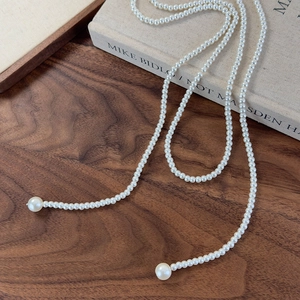 Detail of long white pearl sweater chain on a wooden desk with a vintage book