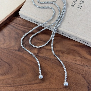 Detailed view of grey long pearl necklace with double drop pendants on vintage wooden background