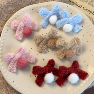 Knitted bow earrings with plush pom poms in multiple colors on a ceramic tray