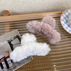 Detail von flauschigen Plüsch-Haarklammern in Weiß und Rosa auf einem Holztisch