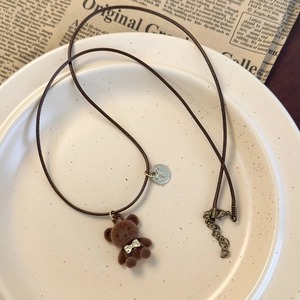 Détail d'un pendentif ours floqué marron avec nœud papillon sur collier cordon