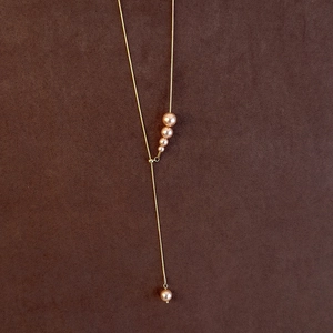Macro detail of elegant Y-shaped gold necklace with gradient purple pearls on brown leather