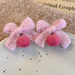 Close-up of pink knitted bow earrings with fluffy faux fur pom-pom drops on ceramic tray
