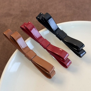 Dettaglio di fermagli per capelli a fiocco in pelle lucida nei colori nero e bordeaux