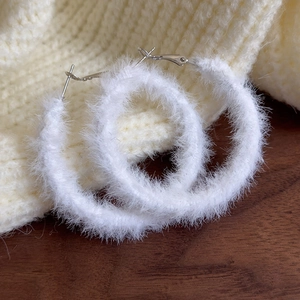 Detailaufnahme der weißen Plüsch-Creolen auf einem warmen Strick-Winterhintergrund