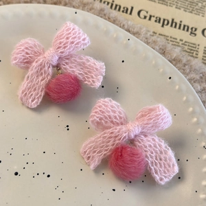 Detail of pink knitted bow earrings with plush pom-poms on a decorative ceramic plate