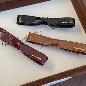 Close-up of three faux leather bow hair clips in black, burgundy, and brown with gold logo