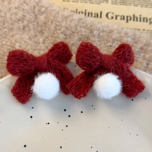 Close-up of red knitted bow hair clips with white pom-poms on a ceramic plate