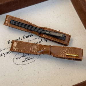Detailed macro view showing the brown leather hair clip texture and gold metal logo