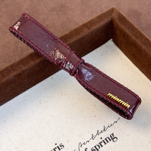 Close-up of wine red glossy patent leather watch strap with stitching and gold logo detail