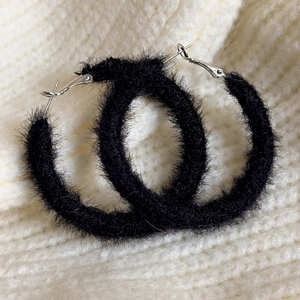 Nahaufnahme von schwarzen Plüsch-Ohrreifen mit weicher Textur auf beigem Strickhintergrund