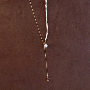 Detail of adjustable Y-shaped pearl necklace featuring gold chain on brown suede surface