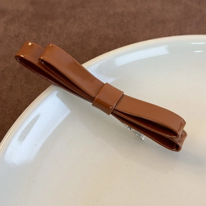 Dettaglio della molletta per capelli a doppio fiocco marrone con finitura lucida e clip a becco