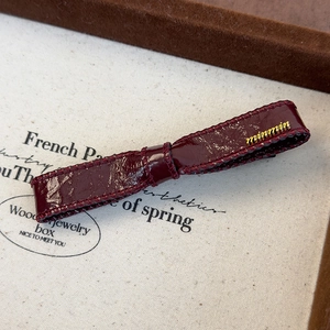 Detailed macro shot of a dark red faux leather bow hair clip with gold metal logo