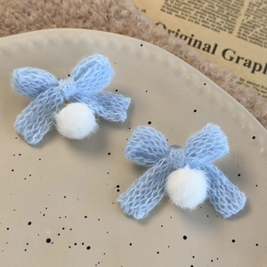 Detail of light blue knitted bow hair clips with white fuzzy pom poms on a ceramic plate