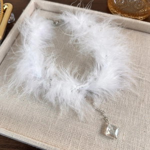 Close-up of white feather choker with square crystal pendant on beige linen display tray