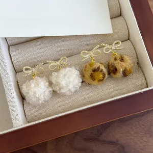 Detail of bow earrings with white and leopard print plush pom poms in jewelry box