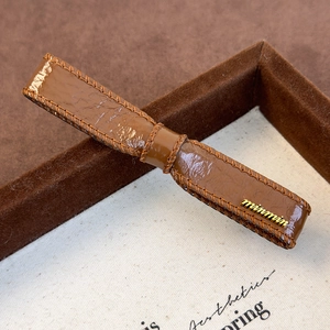 Detail of brown faux leather hair clip with visible stitching and golden minmin logo