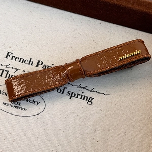 Detail of dark brown faux leather bow clip with golden metal letters and fine stitching