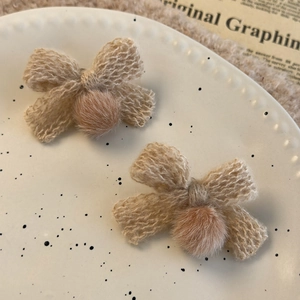 Close-up of beige knitted bow earrings with soft plush pompom on a decorative ceramic tray